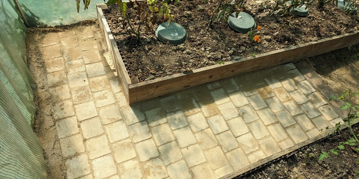 Bacs de culture dans une serre tunnel avec plants de fraisiers et légumes au potager breton.