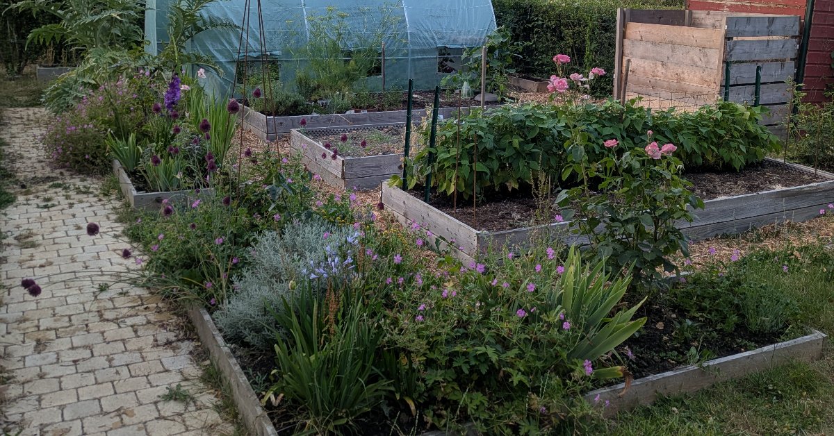 Potager breton en bacs surélevés avec serre tunnel, massifs de fleurs et composteurs en bois.